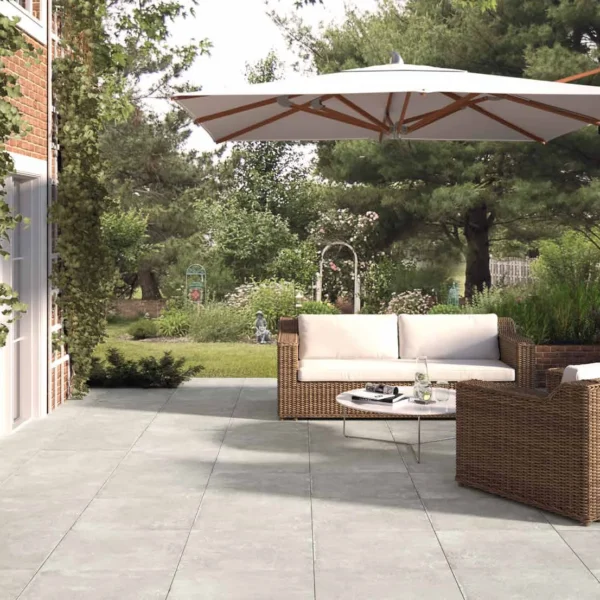 Brick wall with climbing vines and a modern wicker seating set under a white umbrella on a tiled patio.