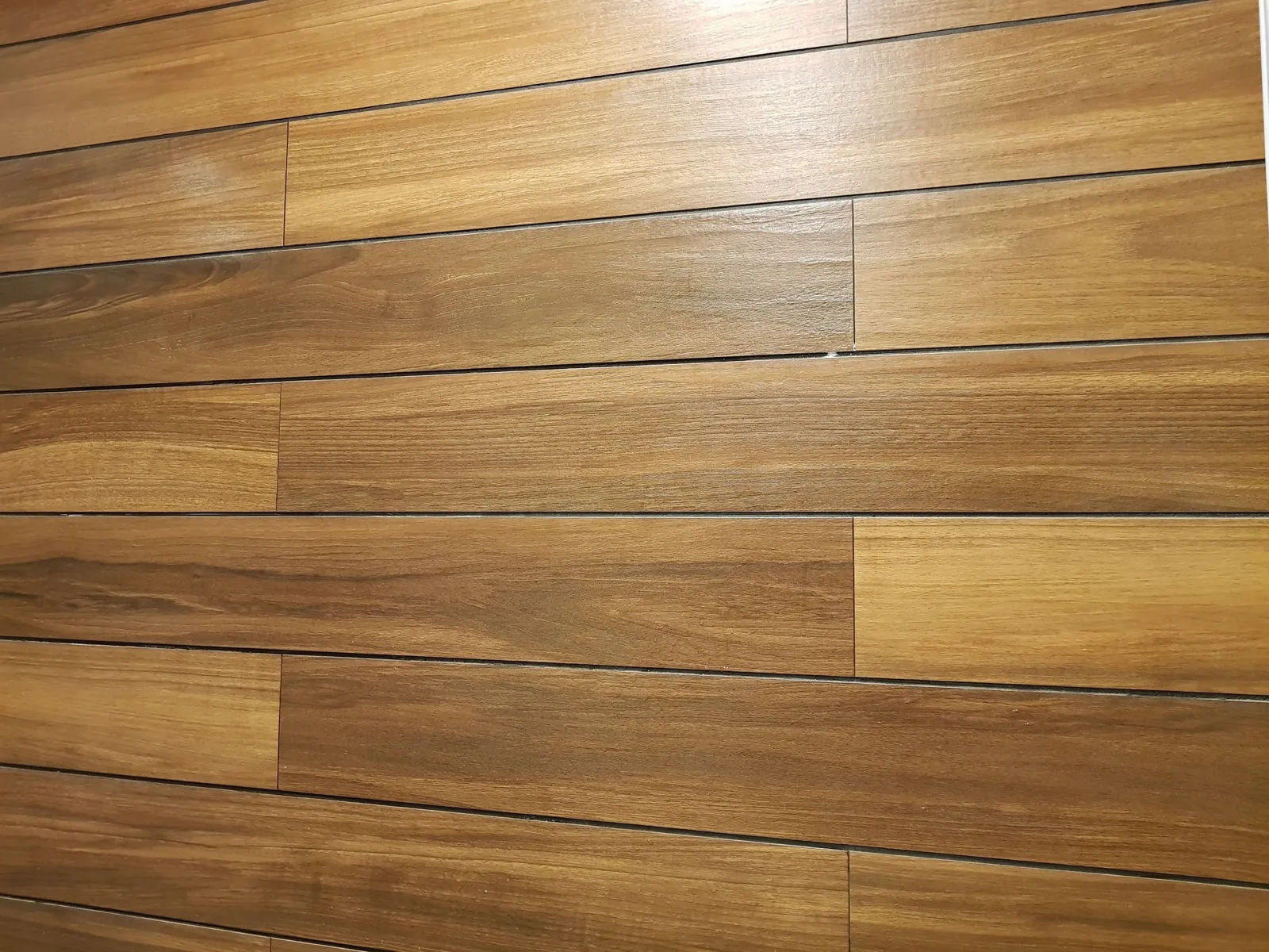 Rosturi inegale între lamele ceramice aspect lemn pe peretele unei băi