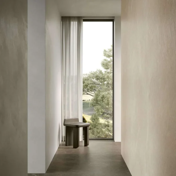 Narrow minimalist hallway with a tall window at the end, sheer curtains, and a small wooden bench beside it, overlooking greenery outside.
