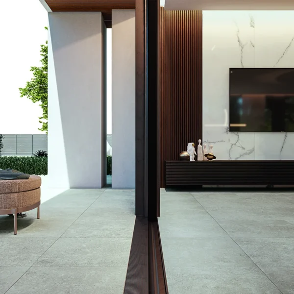 Modern living room with a wall-mounted flat-screen TV on a marble accent wall, a dark wood low console, and an outdoor curved beige seating area visible through glass doors to the left.