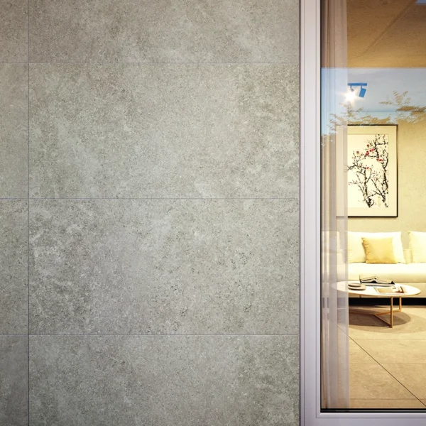 Exterior wall clad in gray stone tiles beside a glass door opening to a living room with a beige sofa, coffee table, and framed artwork.