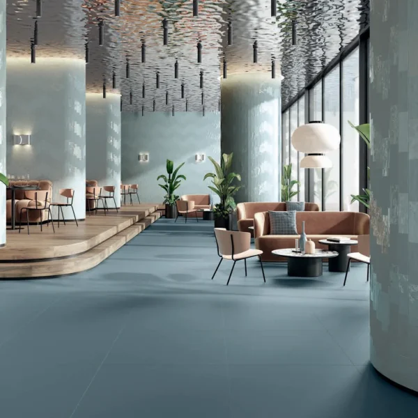 Open, modern hotel lobby with teal tiled walls, curved columns, and lounge seating around round coffee tables in a airy space.