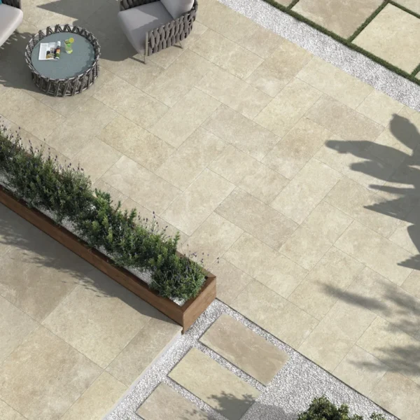 Aerial view of a modern outdoor patio with beige tile flooring, wicker seating, a wooden table, and a planter box with green shrubs.